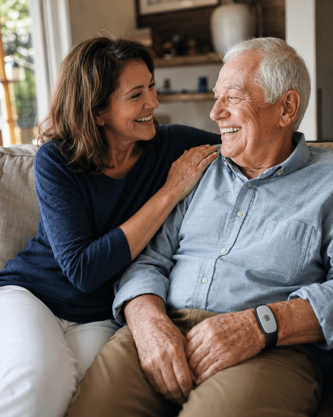 Adult daughter sitting close beside her elderly father, both smiling, at home